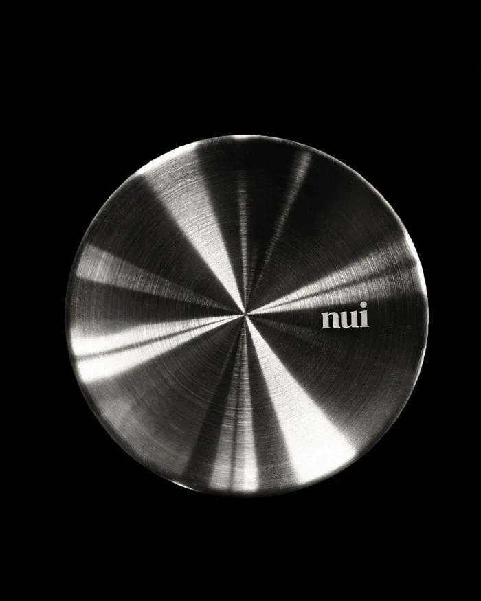 A brushed metal bowl lid engraved with the Nui logo