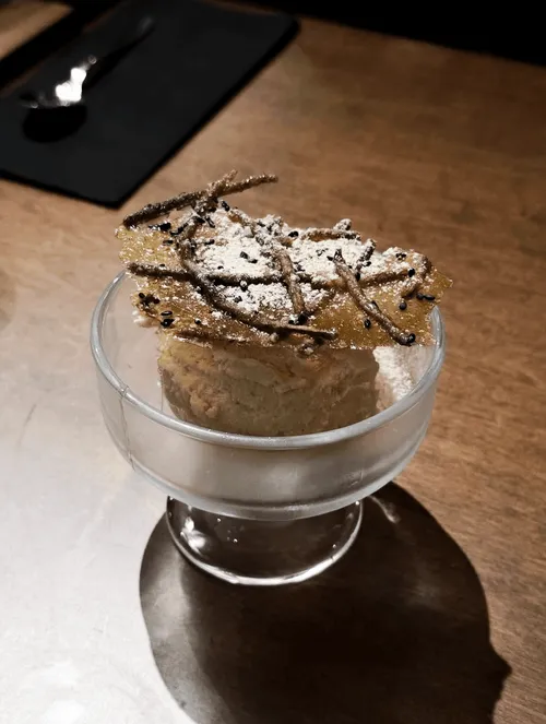 A dessert in a glass cup, topped with a crisp wafer