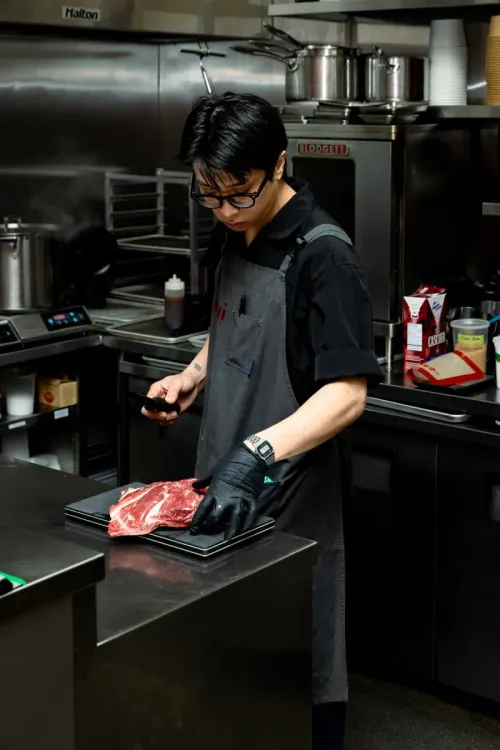 A Nui chef trimming a cut of raw beef in the kitchen