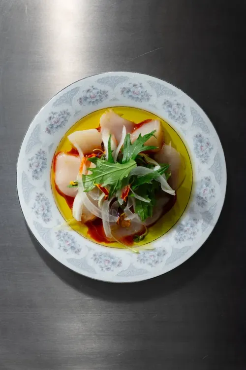 Sliced raw fish in a chili sauce with greens and onion, on a floral plate
