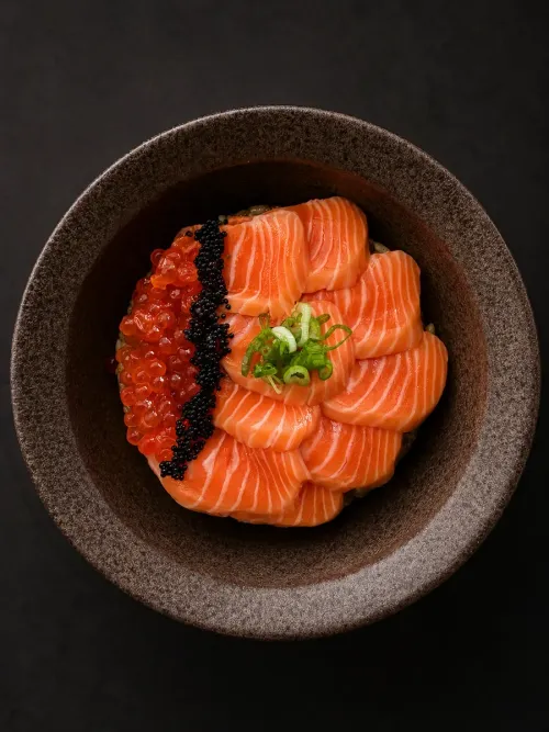 A bowl of sliced salmon over rice with salmon roe and black caviar