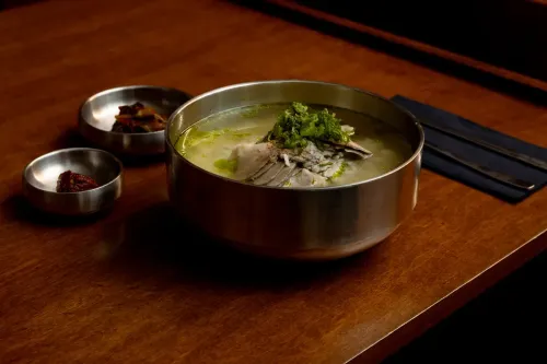 A steel bowl of gomtang beside two small side dishes