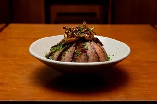Sliced beef topped with mushrooms and chives in a white bowl