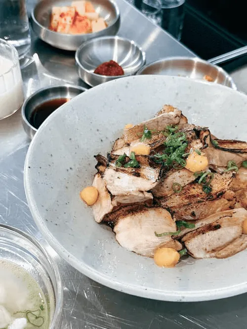 A plate of sliced pork with sides of kimchi and sauces