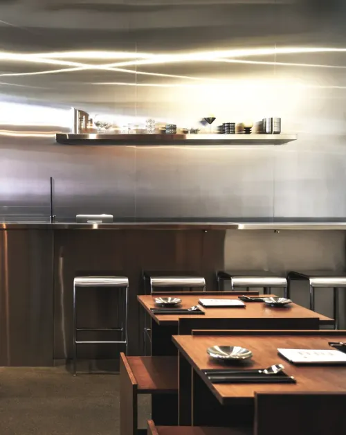 Steel counter stools and wooden tables in front of a brushed steel wall