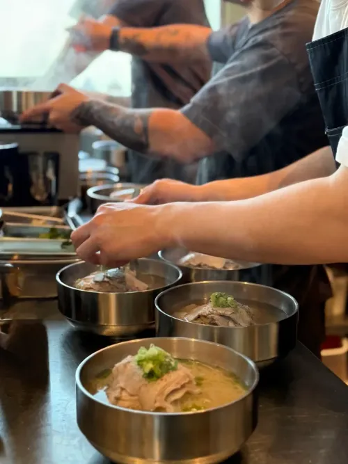 Chefs garnishing steel bowls of gomtang on the line